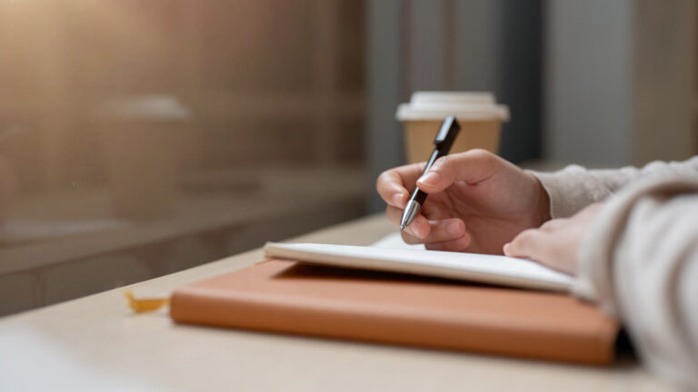 Main de femme écrivant dans un carnet près d'une fenêtre