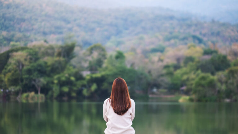 Femme assise au bord d'un lac face aux montagnes, répit
