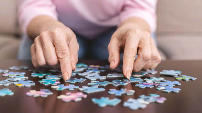 Mains d'une femme âgée assemblant un puzzle