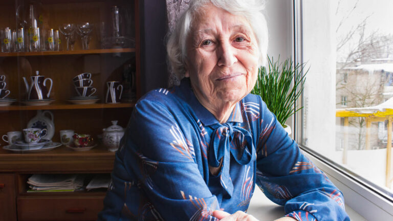 Femme âgée assise seule près de la fenêtre de sa maison