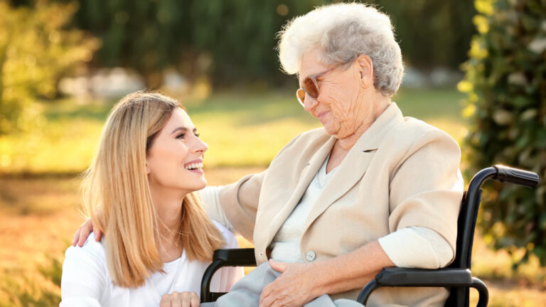 Dame âgée en fauteuil roulant accompagnée d'une soignante dans un jardin