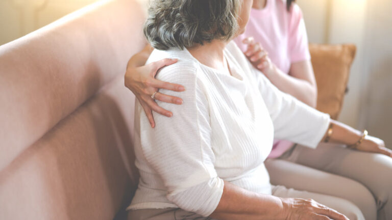 Main d'une aidante posée sur l'épaule d'une femme âgée