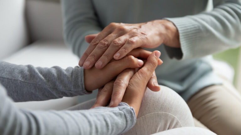 Mère âgée et fille adulte assises main dans la main sur le canapé