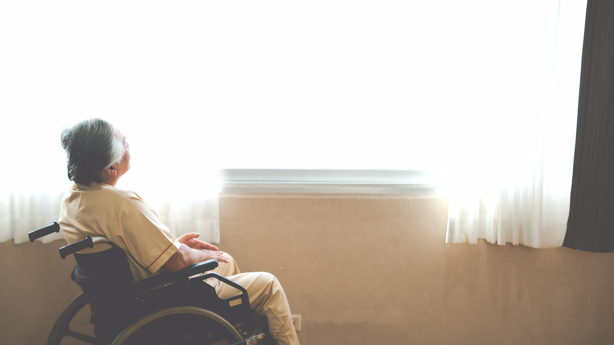 Homme âgé triste en fauteuil roulant regardant par la fenêtre