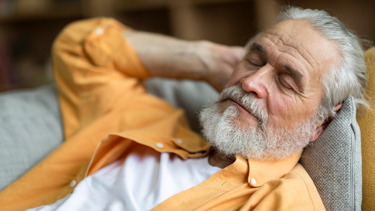Homme âgé endormi sur le canapé en journée