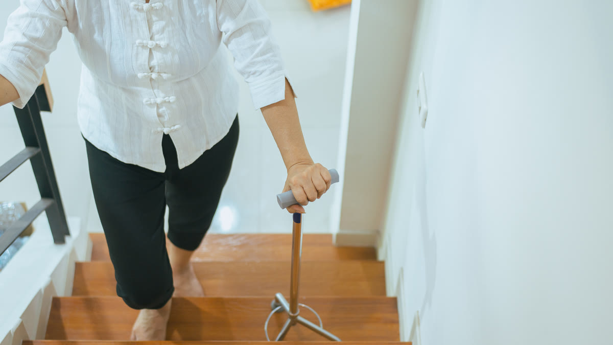 Femme âgée montant l'escalier en se tenant avec des cannes