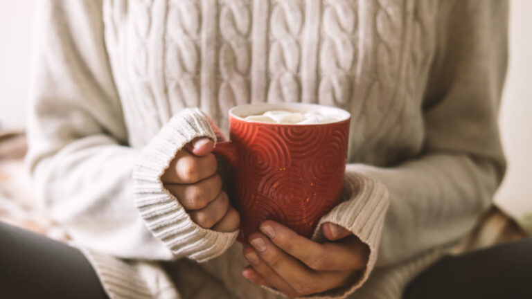 Mains tenant une tasse chaude sous un plaid en hiver