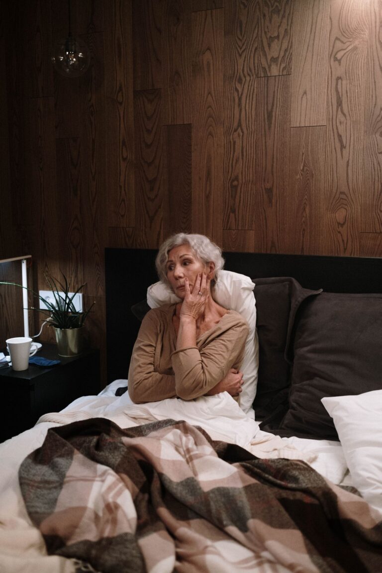Femme âgée assise dans son lit le soir, l'air inquiet, agitation vespérale liée à Alzheimer
