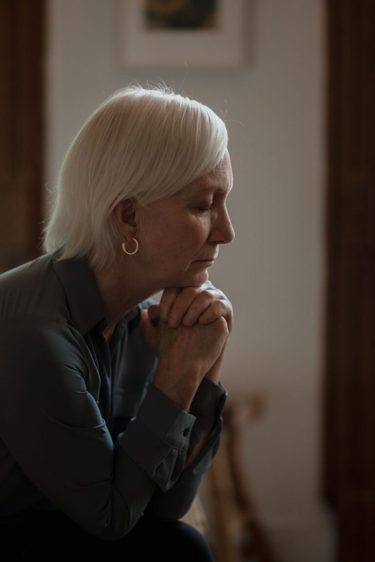 Femme âgée seule et pensive près d'une fenêtre, signes de dépression