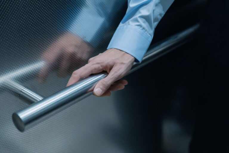 Main d'une personne âgée saisissant une barre d'appui en inox