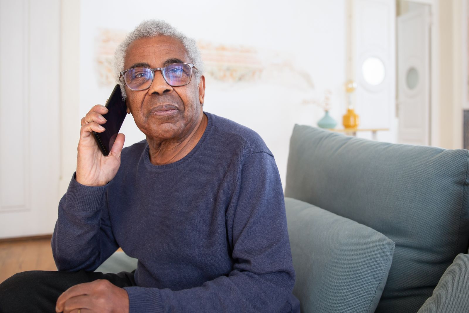 Homme âgé au téléphone depuis son canapé, à son domicile