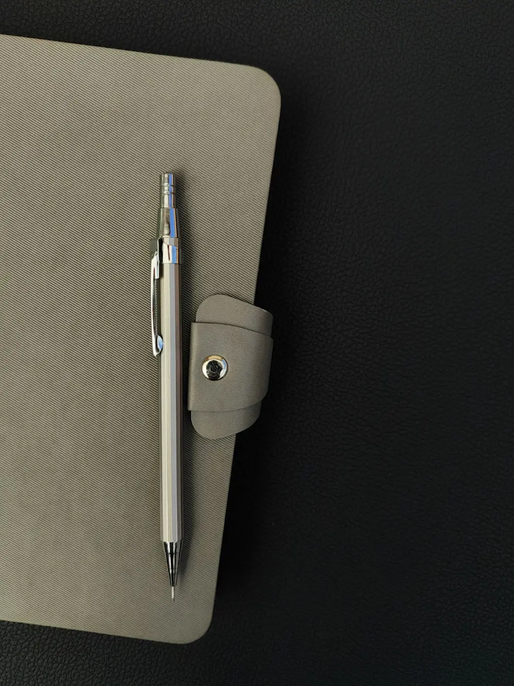 Carnet gris fermé et porte-mine posés sur un bureau sombre