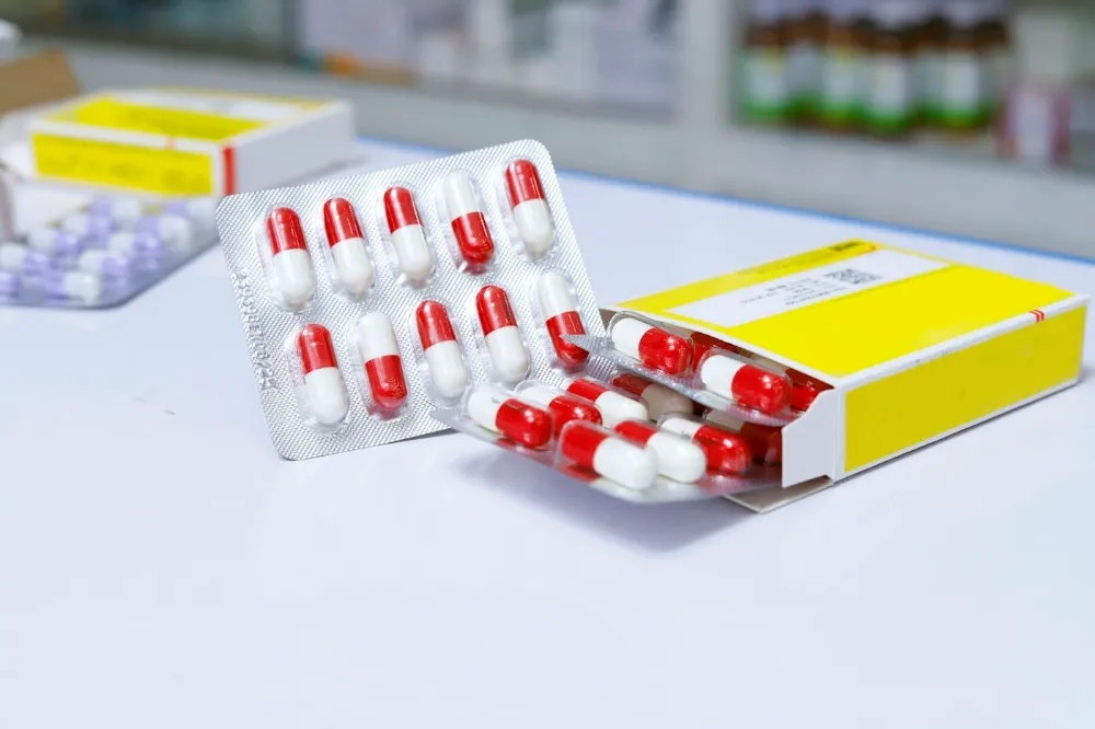 Boîte de médicaments et plaquette de gélules posées sur un comptoir de pharmacie