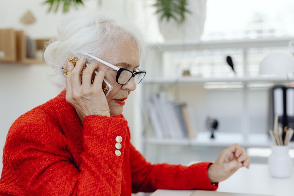 Femme âgée au téléphone devant son ordinateur, vérifiant ses comptes