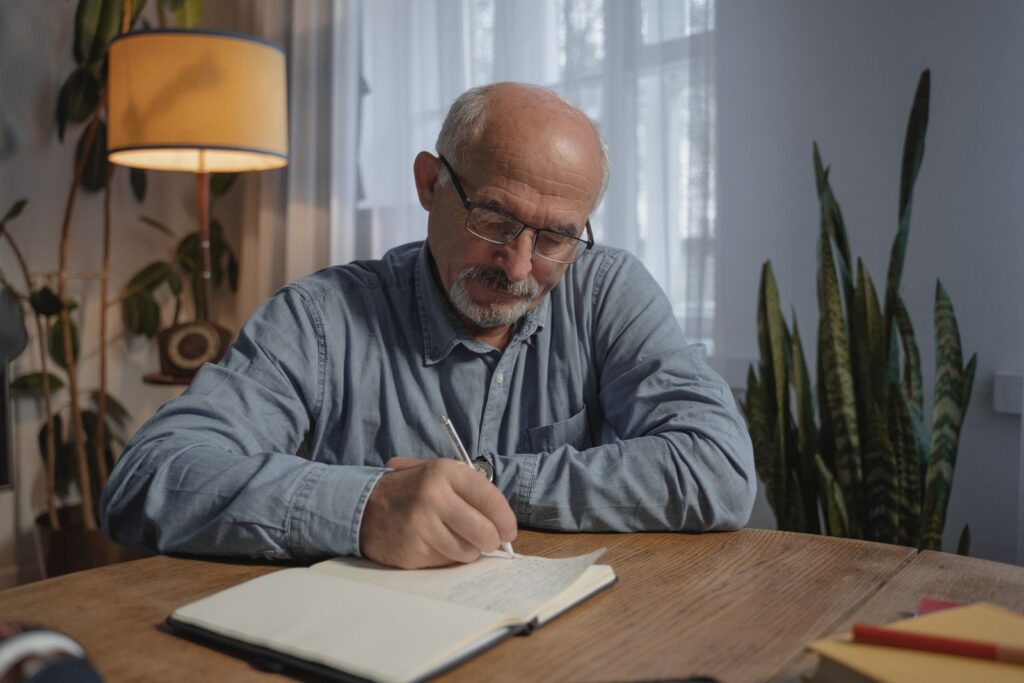 Homme âgé écrivant à la main dans un carnet à son bureau