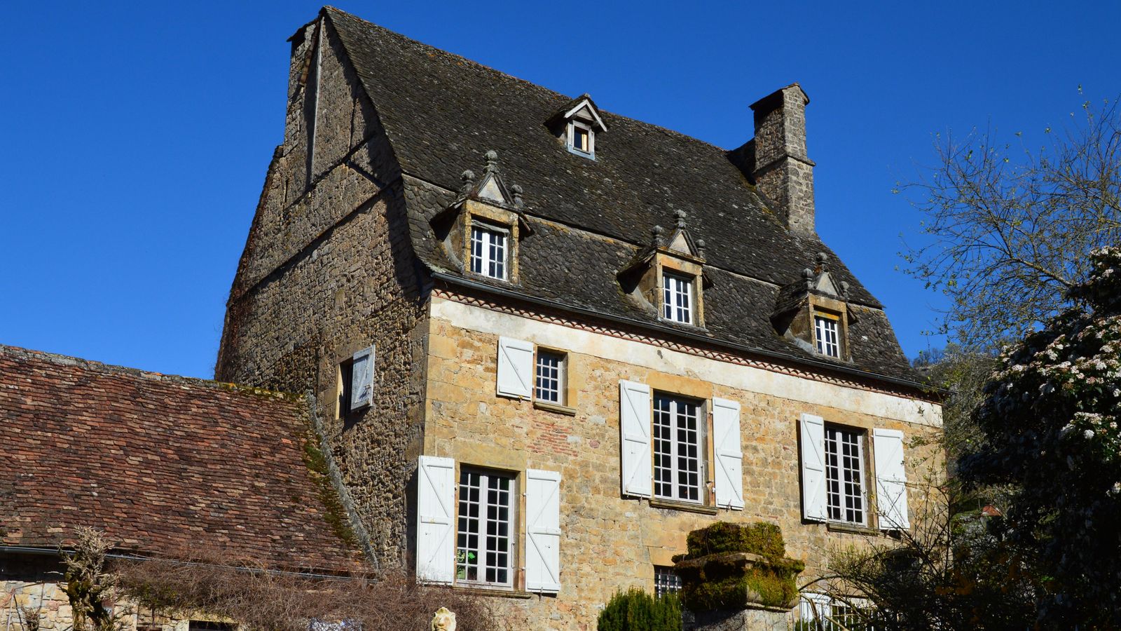 Maison en pierre aux volets blancs sous un ciel bleu